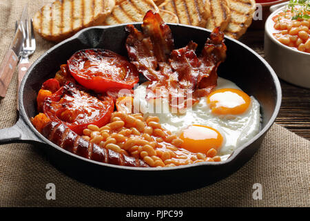 Englisches Frühstück in der Pfanne mit Würstchen, gegrillte Tomaten, Eier, Speck, Bohnen und Toast Brot Stockfoto