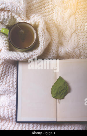 Warme gestrickte Pullover, Tasse heißen Tee und Buch Stockfoto