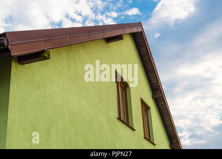 Helle grüne Hausfassade mit sichtbaren Dach Fassade und Fenster. Im Hintergrund einen schönen blauen Himmel mit Wolken. Stockfoto