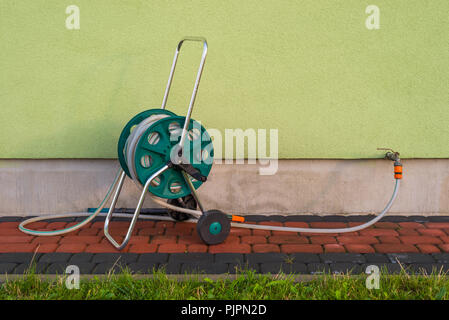 Gartenschlauch zu tippen ragen aus einem Gebäude vor dem hintergrund der grünen Fassade verbunden. Stockfoto