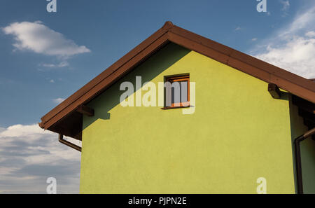 Helle grüne Hausfassade mit sichtbaren Dach Fassade und Fenster. Im Hintergrund einen schönen blauen Himmel mit Wolken. Stockfoto