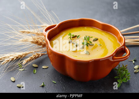 Kürbissuppe mit Thymian Kräuter-, Creme- und Kürbiskernen diente in orange Kürbis geformte Schale Stockfoto