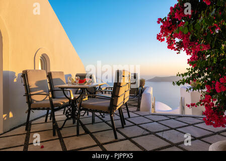 Terrasse mit Tisch und Stühlen mit wunderschönen Bougainvillea Blumen auf der Insel Santorin, Griechenland Stockfoto