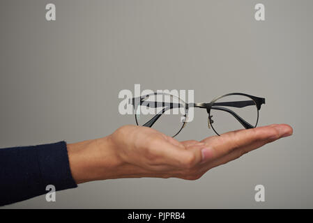 Holding Brille auf der Handfläche close-up auf grauem Hintergrund Stockfoto