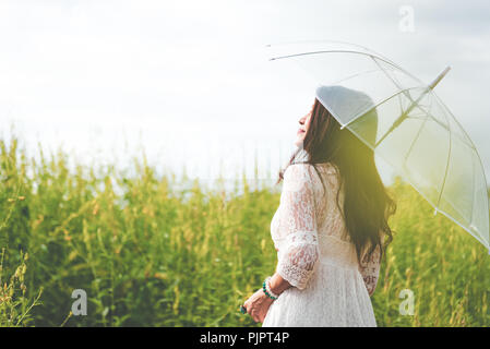 Beauty asiatische Frau in weißem Kleid Holding transparent Regenschirm und Blick auf Himmel zwischen Raps Blüte Feld Hintergrund. Menschen Entspannung und Reisen Stockfoto