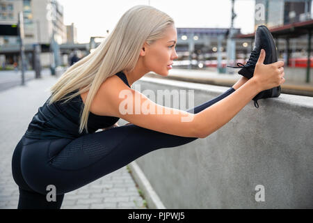 Entschlossene junge Frau Stretching Bein auf dem Geländer in Stadt Stockfoto