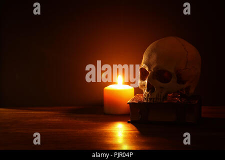 Menschlicher Schädel, altes Buch und brennende Kerze über alten Holztisch und dunklen Hintergrund Stockfoto