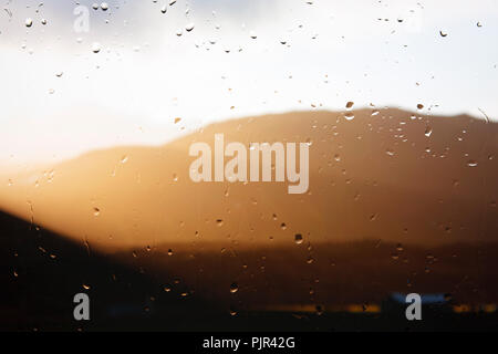 Sonnenlicht bricht durch die Wolken durch ein Regentropfen fallen Fenster gesehen. Stockfoto