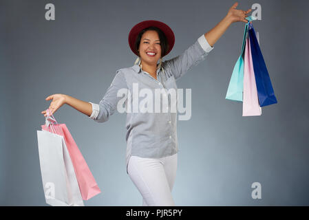 Gerne Frau mit bunten Einkaufstaschen auf Grau studio Hintergrund isoliert Stockfoto