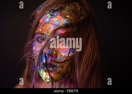 Studio headshot von Gesicht einer Frau in farbigen Pulver unter eine ultraviolette Licht Stockfoto