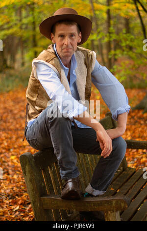 Ein Mann, gekleidet wie ein Cowboy, nimmt einen Bruch sitzt auf einer Holzbank, Stockfoto