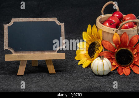 Schönen Herbst und im Herbst Szene mit einem Korb Äpfel, bunte Sonnenblumen und leere Schiefertafel für Ihre Nachricht. Schwarzer Hintergrund Stockfoto