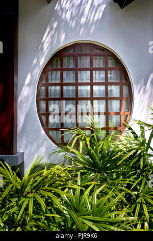 Japanisches Fenster. Rundes Fenster mit Holzpaneellen in einer weißen Wand Stockfoto