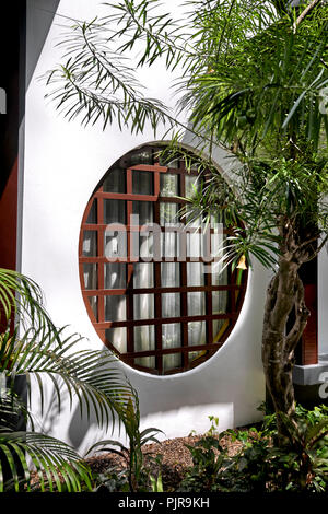 Japanisches Fenster. Rundes Fenster mit Holzpaneellen in einer weißen Wand Stockfoto