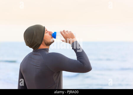 Zweiter Mann Getränke Wasser aus der Flasche gegen Meer Hintergrund Stockfoto