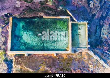 Overhead Luftaufnahme unten zu Mona Vale rock Pool mit Schwimmen Mann im Meer Wasser vom Pazifischen Ozean Flut über sandsteinfelsen Plateau. Stockfoto