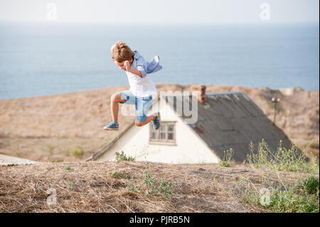 Gesunde, aktive kaukasische Zicklein springen hoch auf einem Hügel im alten Haus und Meer Küste Hintergrund Stockfoto