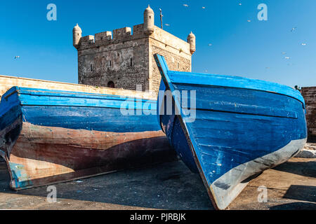 Zwei blaue Fischerboote sind auf einem Dock am Fuße der Zitadelle von Mogador in Essaouira in Marokko Litze Stockfoto