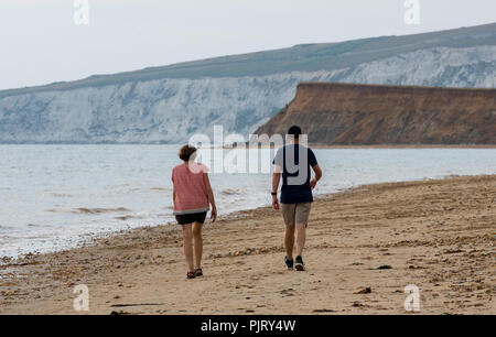 Mann und Frau oder Paar entlang eine sandige windigen Strand auf der Isle of Wight mit Landschaft und Felsen im Hintergrund. Stockfoto