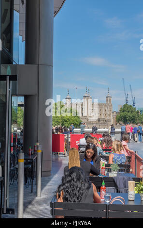 Diners und Menschen essen auf der Terrasse eines Restaurants an mehr London Riverside in London mit dem Tower von London in der Ferne. Stockfoto