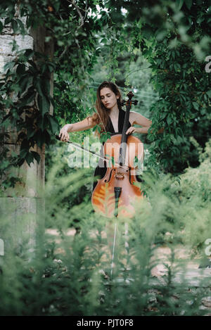 Eine junge, blonde Frau in einem schwarzen Kleid steht ein Cello spielen unter einem Torbogen ruiniert Stockfoto