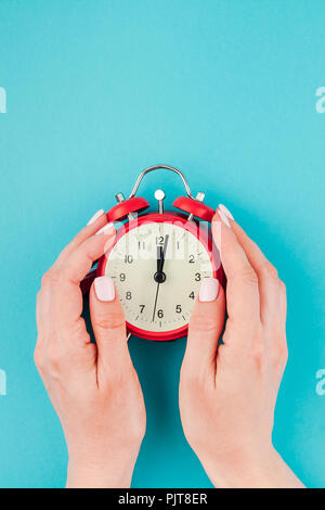 Kreative flach Konzept top Blick auf Frau Hände halten der Roten vintage Wecker auf hellen blau türkis Farbe Papier Hintergrund mit Kopie Raum Stockfoto