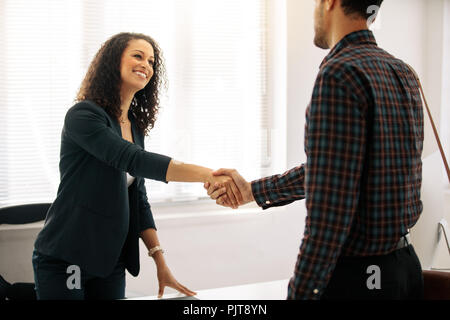 Geschäftspartner treffen im Büro zitternden Hand. Frau Unternehmer in formelle Kleidung Gruß ein Geschäftsmann an ihrem Tisch im Amt. Stockfoto