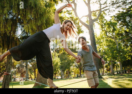 Frau tun Schlaffseil wandern in einem Park. Mann hilft Frau in Balancing während ihrer Gratwanderung in einem Park. Stockfoto