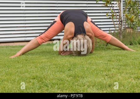 Attraktive ältere blonde Frau als Vorläufer Ihr erstreckt sich in einer tiefen Verbeugung berühren den Rasen mit ihren Armen und ihren Kopf Stockfoto
