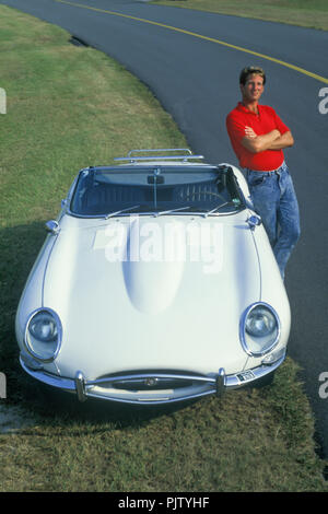 1990 HISTORISCHER MANN, DER ALLEIN AUF DEM STRASSENGRAS STEHT, MIT DEM WEISSEN CABRIOLET XK-E E-TYPE JAGUAR (©JAGUAR CARS LTD 1961) DER SERIE 1966 DER SERIE 1 Stockfoto