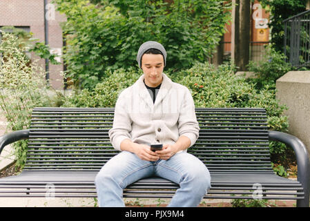 Junger Mann texting Während sitzt auf der Bank, Vancouver, Kanada Stockfoto