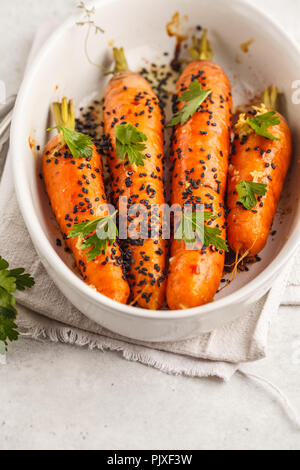 Ganze junge Karotten gebacken mit asiatischen Soße und Sesam seedsin weiße Schale. Stockfoto