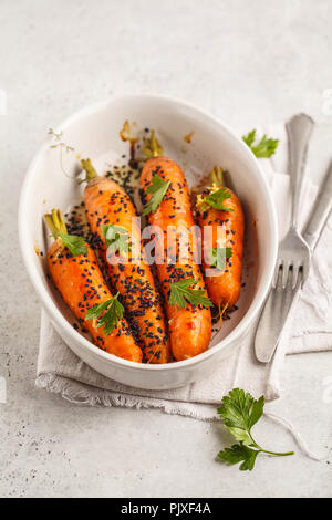 Ganze junge Karotten gebacken mit asiatischen Soße und Sesam seedsin weiße Schale. Stockfoto
