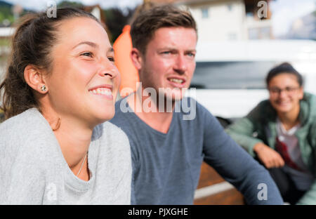Mehrere junge männliche und weibliche Personen sitzen auf einer Bank und lächelnd und Beobachten ein Spiel Stockfoto