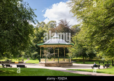 Hexham, Northumberland. Ein musikpavillon mit kunstvollen Schmiedearbeiten und ein spitzes Dach steht durch einen Pfad und Bänken umgeben. Es ist von alten Bäumen eingerahmt. Stockfoto