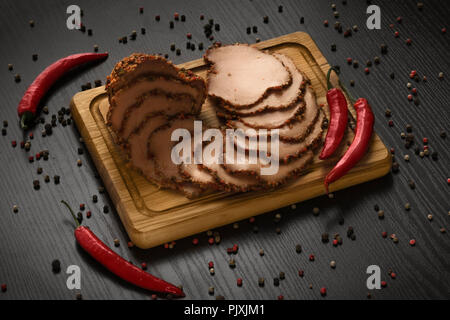 Scheiben Schinken auf Holzbrett mit rotem Pfeffer closeup Stockfoto