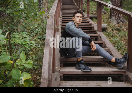 Junge Mann sitzt auf der Treppe im Wald Stockfoto