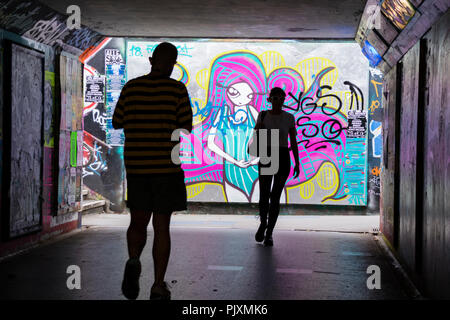 Mann hinter einer Frau in einer Bristol Fußgängertunnel mit Graffiti, Stadt Bristol, England, Großbritannien Stockfoto