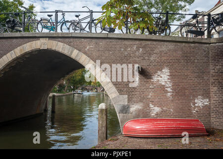 Ein rotes Ruderboot liegt am Ufer des Oude Gracht in Utrecht, Niederlande an einem sonnigen Tag im frühen Herbst. Stockfoto