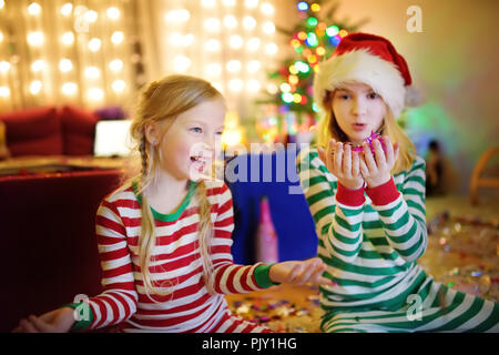 Zwei adorable Schwestern feiern Silvester in schön eingerichteten Zimmer wie zu Hause. Spaß für die ganze Familie unter dem Weihnachtsbaum auf wunderbare Weihnachtszeit. Stockfoto