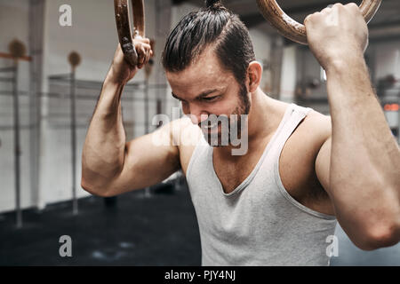 Passen junge Mann in Sportkleidung lächelnd, während Sie arbeiten einen Schweiß beim Training Session mit Ringen an der Turnhalle Stockfoto