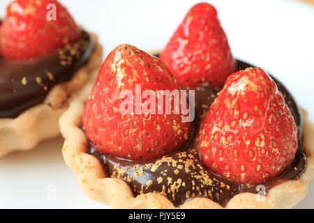 Nahaufnahme der Schokoladentorte garniert mit frischen Erdbeeren und genießbare gold Pulver auf weiße Platte serviert. Stockfoto