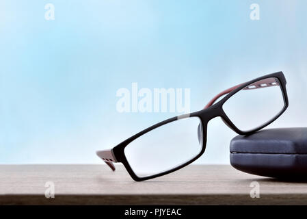 Brillen mit Etui auf Holz Tisch mit blauen Hintergrund in einem eyewear Store. Vorderansicht. Horizontale Zusammensetzung Stockfoto