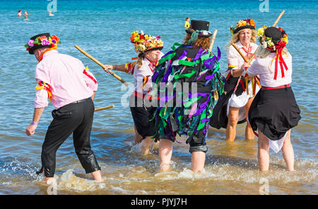 Swanage, Dorset, Großbritannien. 9. September 2018. Menschenmassen strömen zu den zweiten Tag der Swanage Folk Festival der Tanzgruppen und Musik entlang der Küste zu sehen. Herrlich warme sonnige Wetter lockte einige Tänzer im Meer, am Ende einer wunderschönen Wochenende zu tanzen. Morris Dancers, Mitglieder von Phoenix Morris tanzen im Meer mit Mitglied von Wicket Brut Grenze Morris. Credit: Carolyn Jenkins/Alamy leben Nachrichten Stockfoto