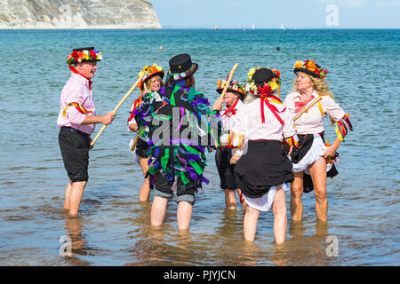 Swanage, Dorset, Großbritannien. 9. September 2018. Menschenmassen strömen zu den zweiten Tag der Swanage Folk Festival der Tanzgruppen und Musik entlang der Küste zu sehen. Herrlich warme sonnige Wetter lockte einige Tänzer im Meer, am Ende einer wunderschönen Wochenende zu tanzen. Morris Dancers, Mitglieder von Phoenix Morris tanzen im Meer mit Mitglied von Wicket Brut Grenze Morris. Credit: Carolyn Jenkins/Alamy leben Nachrichten Stockfoto