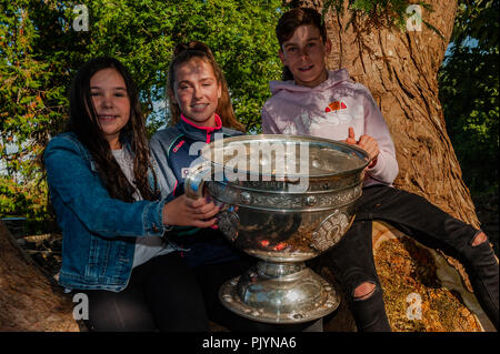 Dunmanway, West Cork, Irland. 9. September 2018. Im Rahmen der Sam Maguire Wochenende, mit einem Fall wurde an Malabracka, der Sam Maguire Homestead statt. Die Sam Maguire Cup fand sich in einige seltsame Orte auf der Veranstaltung, dieser Baum ist einer davon. Abgebildet mit der Schale sind Amy Thomson, Dunmanway und Megan und Jack Mallon aus Kork. Credit: Andy Gibson/Alamy Leben Nachrichten. Stockfoto