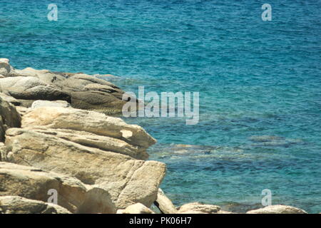 Das kristallklare blaue Wasser der Ägäis, in der Bucht Mylopotos auf der schönen griechischen Insel iOS. Felsen am Ufer. Stockfoto