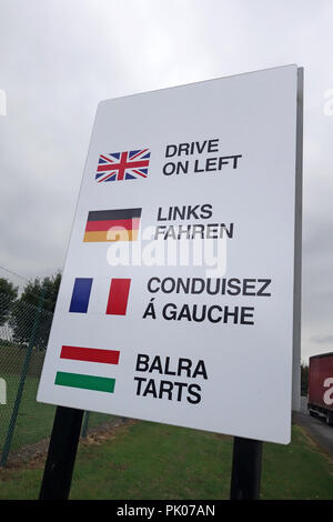 Weiße fahren Sie auf der linken Seite Schild mit Union Jack Flagge und andere Flaggen und Worte in ihrer Sprache als auf britischen Straßen gesehen. Stockfoto