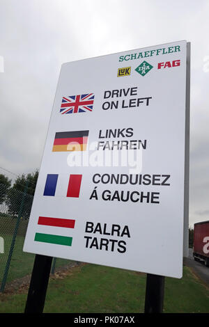 Weiße fahren Sie auf der linken Seite Schild mit Union Jack Flagge und andere Flaggen und Worte in ihrer Sprache als auf britischen Straßen gesehen. Stockfoto