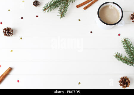 Weihnachten Komposition. Rahmen der Tanne, Fichte Äste, Tannenzapfen, Zimtstangen und glitzernden Konfetti Sterne auf weiße Holztisch Hintergrund. Kaffee in Emaille Tasse. Flach, Ansicht von oben. Stockfoto